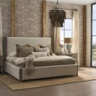 A contemporary upholstered bed in soft beige fabric with a tall padded headboard and natural wood trim accents on the corners and legs.