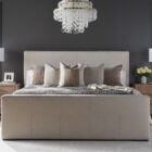 A modern upholstered bed in a soft beige fabric with clean lines, a low-profile footboard, and a tall rectangular headboard.