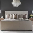 A modern upholstered bed in a soft beige fabric with clean lines, a low-profile footboard, and a tall rectangular headboard.
