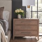 A three-drawer nightstand in a light natural wood finish with sleek horizontal metal handles and tapered legs.