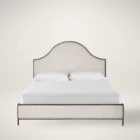 An upholstered bed in soft cream fabric with an arched headboard outlined by a slim dark metal frame, paired with a matching upholstered footboard.
