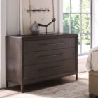 A four-drawer chest in a dark textured wood finish with elongated brass handles and slim tapered legs.