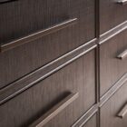 A six-drawer dresser in a dark textured wood finish with long horizontal brass handles and slim tapered legs.