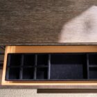 A six-drawer dresser in a dark textured wood finish with long horizontal brass handles and slim tapered legs.