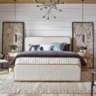 A contemporary upholstered bed with soft cream fabric panels framed by light natural wood, featuring rounded corners and a modern profile.