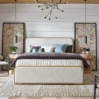 A contemporary upholstered bed with soft cream fabric panels framed by light natural wood, featuring rounded corners and a modern profile.