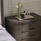 A dark wood nightstand with three drawers, slim black metal handles, and a bold plinth base for a modern grounded look.
