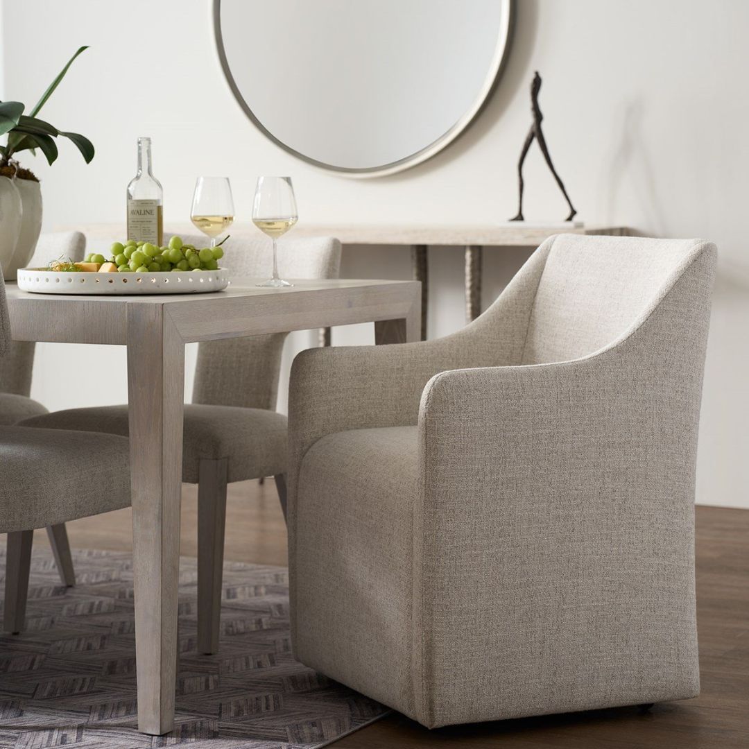 Contemporary upholstered dining chair in soft neutral fabric with clean lines, low arms, and a fully skirted base.