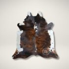 Natural brindle cowhide rug featuring deep brown and black tones with a striking white backbone and organic edges.