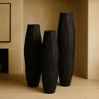 Set of three tall matte black vases with organic carved texture and sculptural, elongated silhouettes.