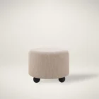 Round beige pouf with textured upholstery and rounded black feet.