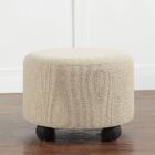 Round beige pouf with textured upholstery and rounded black feet.