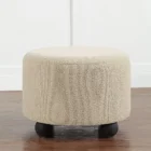 Round beige pouf with textured upholstery and rounded black feet.
