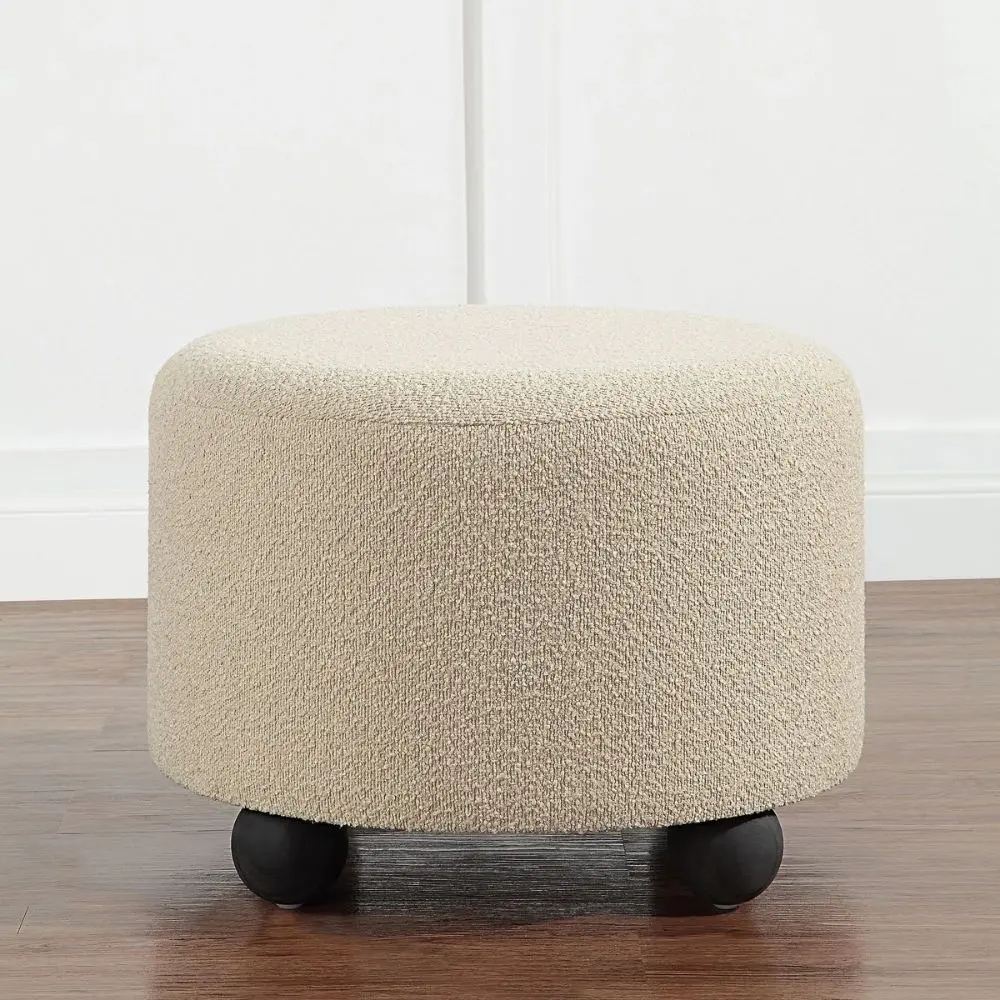 Round beige pouf with textured upholstery and rounded black feet.