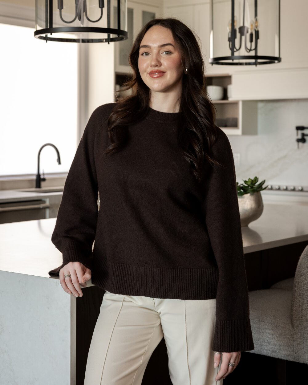 Erin Groulx, interior design assistant at Urbanhome Interior Design, standing in a custom kitchen with black-metal pendant lighting.