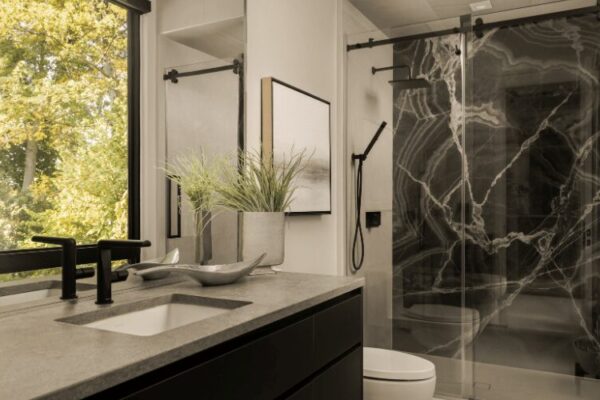 Modern bathroom with stone countertop vanity and glass shower enclosure in lakefront home designed by Urbanhome Interior Design
