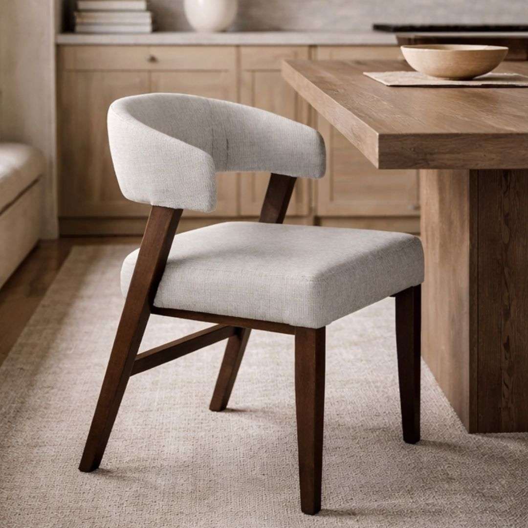 Upholstered dining chair with a curved wraparound back, light neutral fabric, and solid wood legs in a warm brown finish.