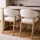 Upholstered dining chair with a curved wraparound back, light neutral fabric, and solid wood legs in a warm brown finish.