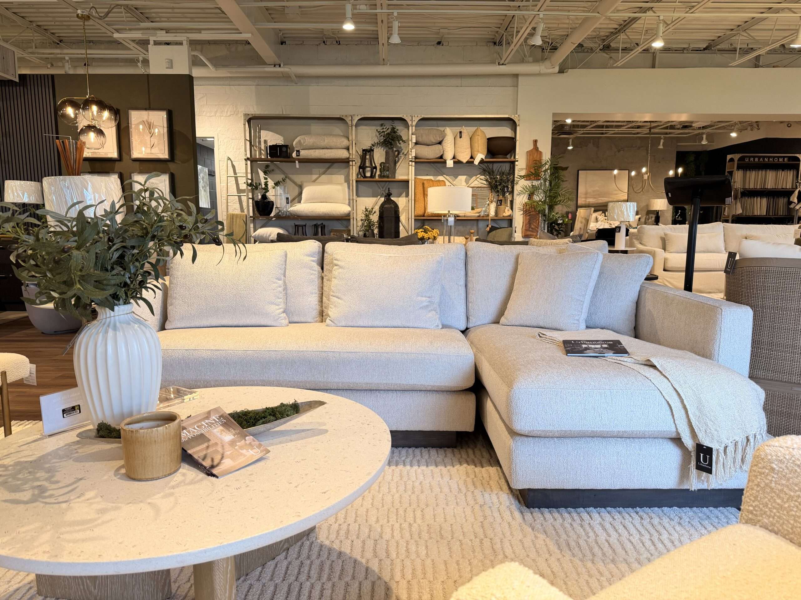 Luxury cream sectional sofa with chaise, round oak coffee table, textured area rug, and curated home décor styled inside Urbanhome Interior Design’s furniture showroom in Windsor, Ontario.