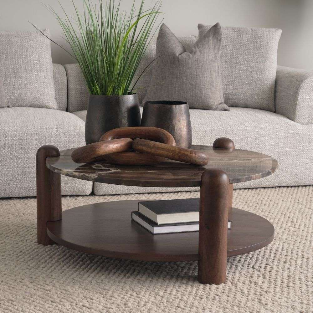 Round coffee table with a natural marble top in warm brown and cream veining, supported by sculptural wood legs and a matching lower shelf.
