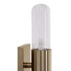 Modern wall sconce with brass backplate and vertical ribbed glass light tubes creating a soft ambient glow.