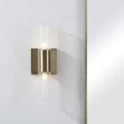 Modern wall sconce with brass backplate and vertical ribbed glass light tubes creating a soft ambient glow.