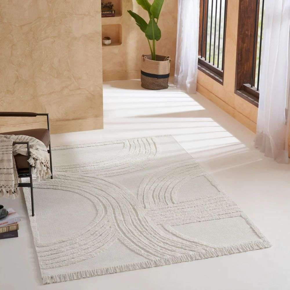 Cream textured area rug with raised geometric patterns and subtle fringe detailing along the edges.