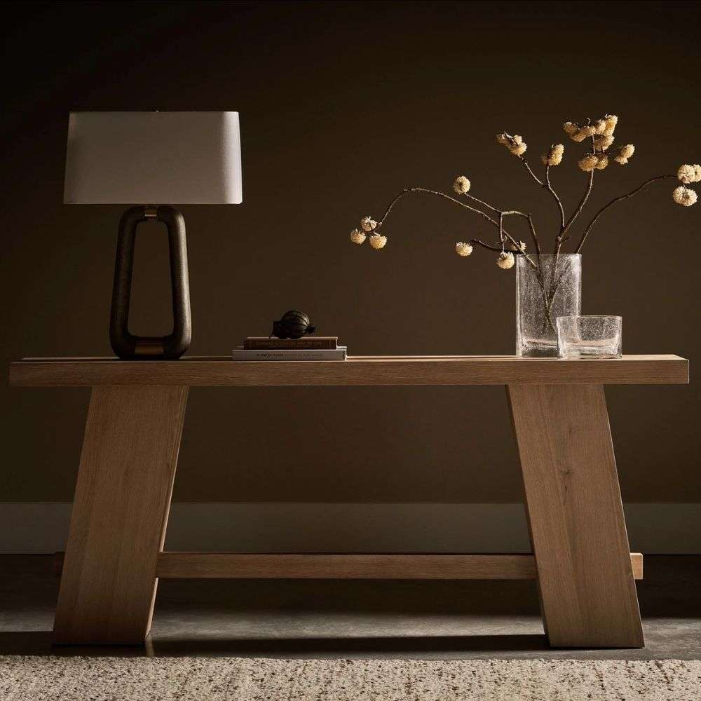 Minimalist wood console table with a rectangular top, angled plank legs, and a lower stretcher in a light natural finish.
