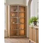 Tall wood display cabinet with arched top, glass-paneled double doors, and interior shelving with warm lighting.