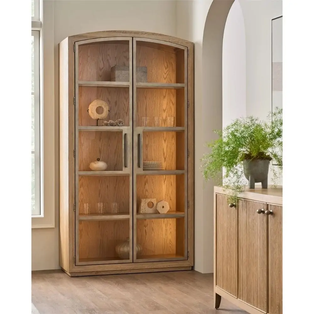 Tall wood display cabinet with arched top, glass-paneled double doors, and interior shelving with warm lighting.