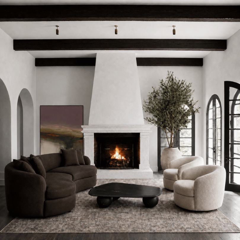 European-inspired living room with a curved brown sofa, cream accent chairs, sculptural coffee table and stone fireplace.