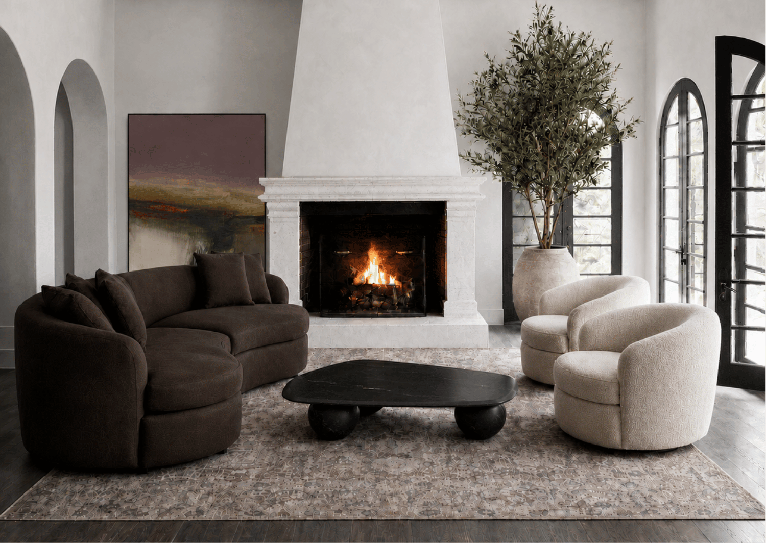 European-inspired living room with a curved brown sofa, two cream bouclé chairs, a sculptural black coffee table and a stone fireplace.