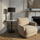 Black marble table lamp styled on a round side table beside a cream armchair and stone fireplace.